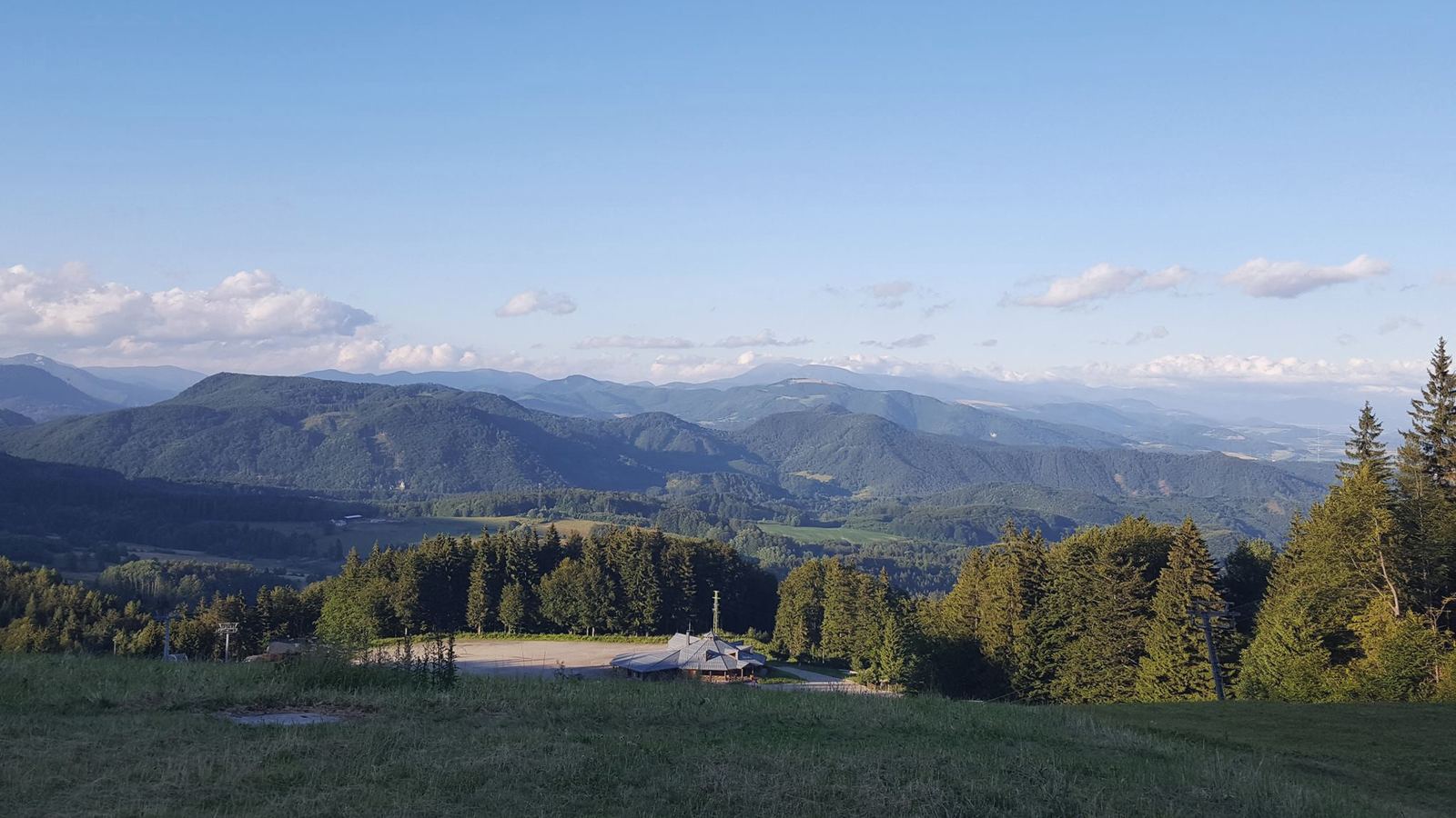 Letný výhľad z lúky nad penziónom: lesy klesajú k hrebeňom, ktoré sa na obzore vrstvia jeden za druhým.