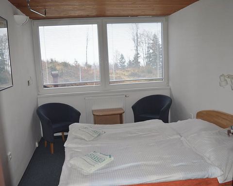 Dvojlôžková izba, pod oknom dve kreslá a stolík.